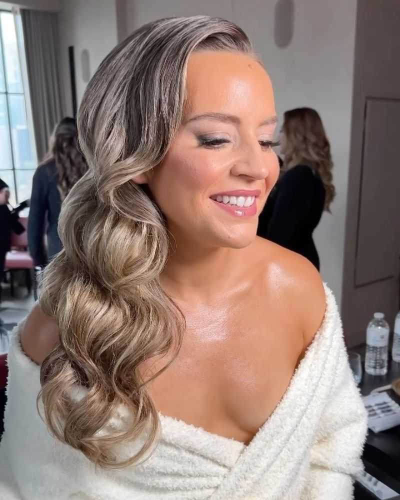 Woman with styled hair and makeup, smiling in a dressing room setting.