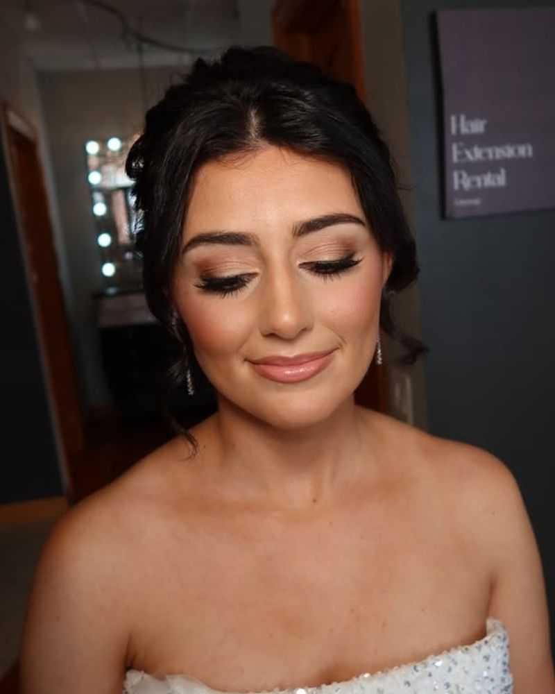 Brunette bride with elegant makeup and strapless gown, eyes closed, in beauty salon.